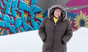 Julie Garreau in the snow and winter coat in front of graffiti art on wall