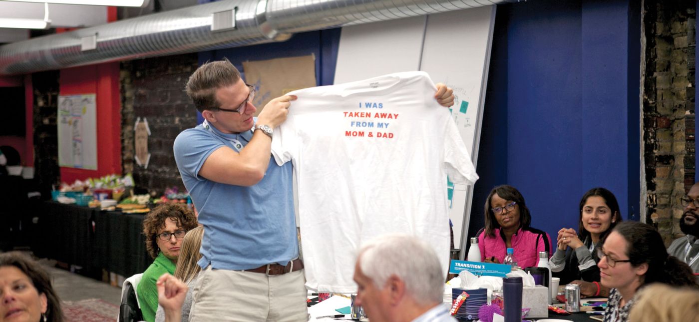 Man holding a t-shirt at the Ten for Ten conference that reads "I was taken away from my mom and dad"
