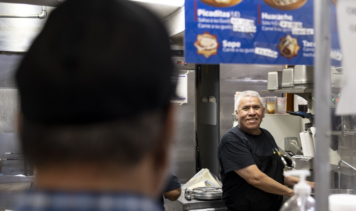 man smiles at a customer from kitchen as customer waits at the service counter