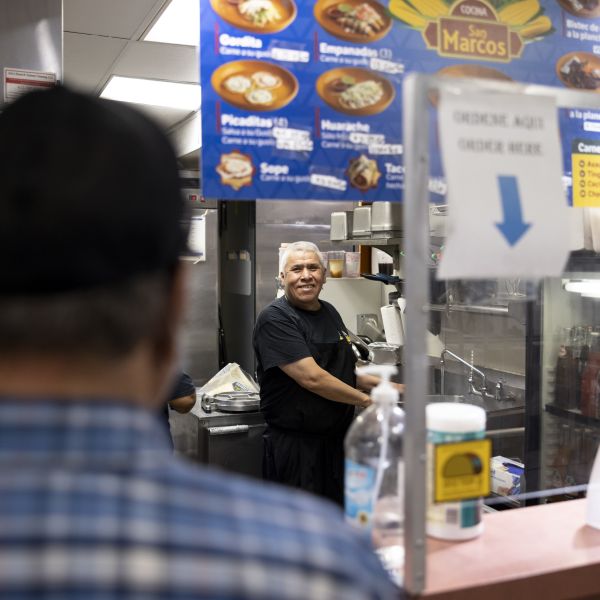 man smiles at a customer from kitchen as customer waits at the service counter