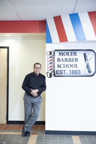 man stands in front of barber shop sign